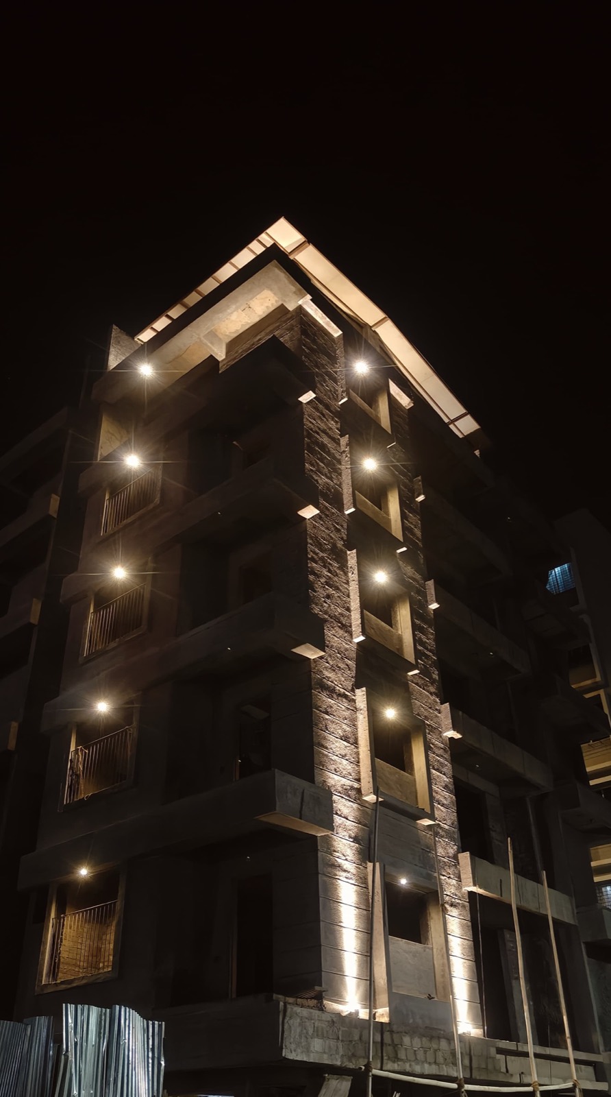 Katariya Urban Leaf at night — external plaster with a stone-clad corner and facade lighting in place, Panchvati, Nashik